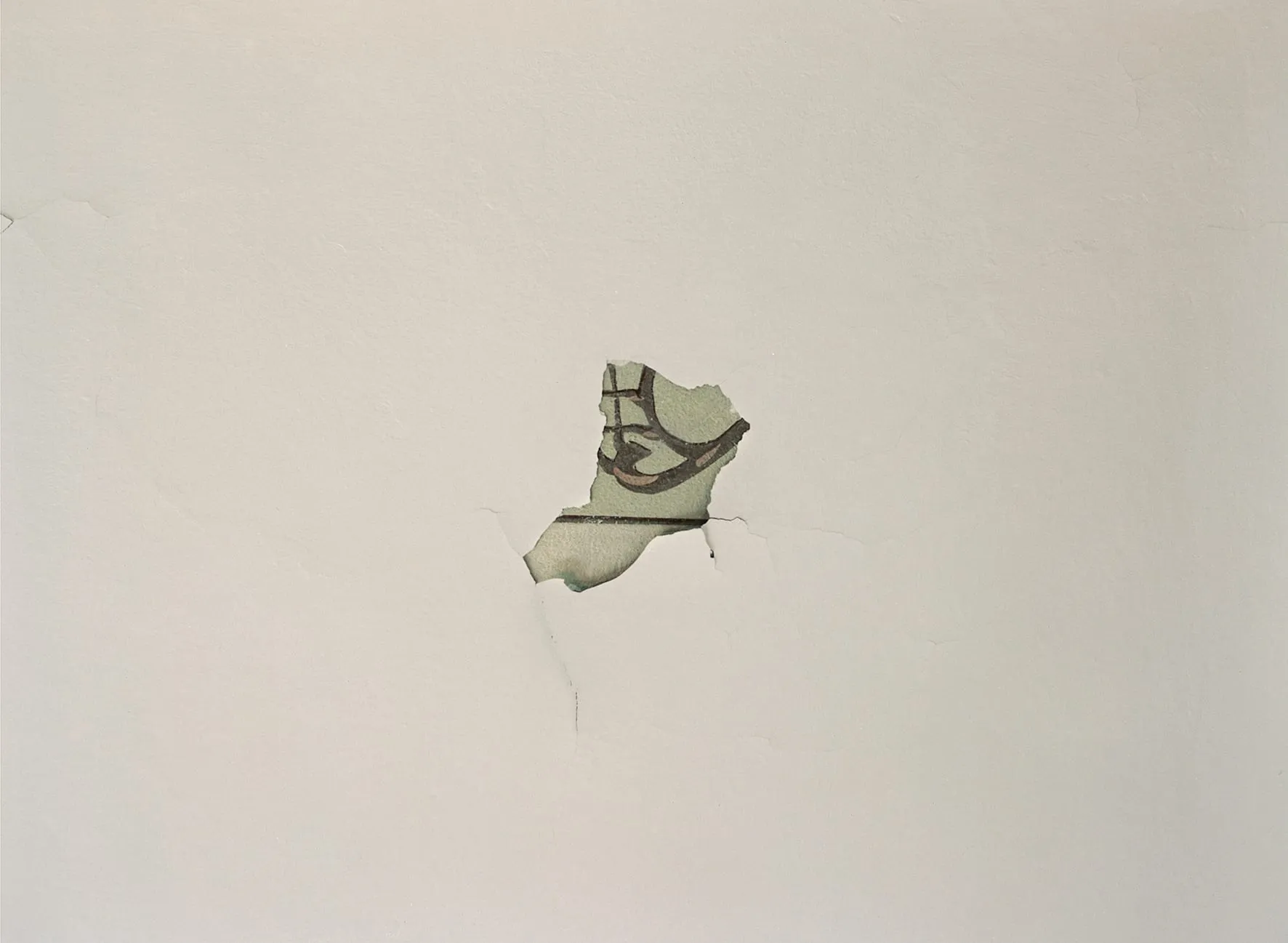 A pale plaster wall where a patch has fallen away, uncovering an older painted layer beneath: pale green ground crossed by dark curved strokes.