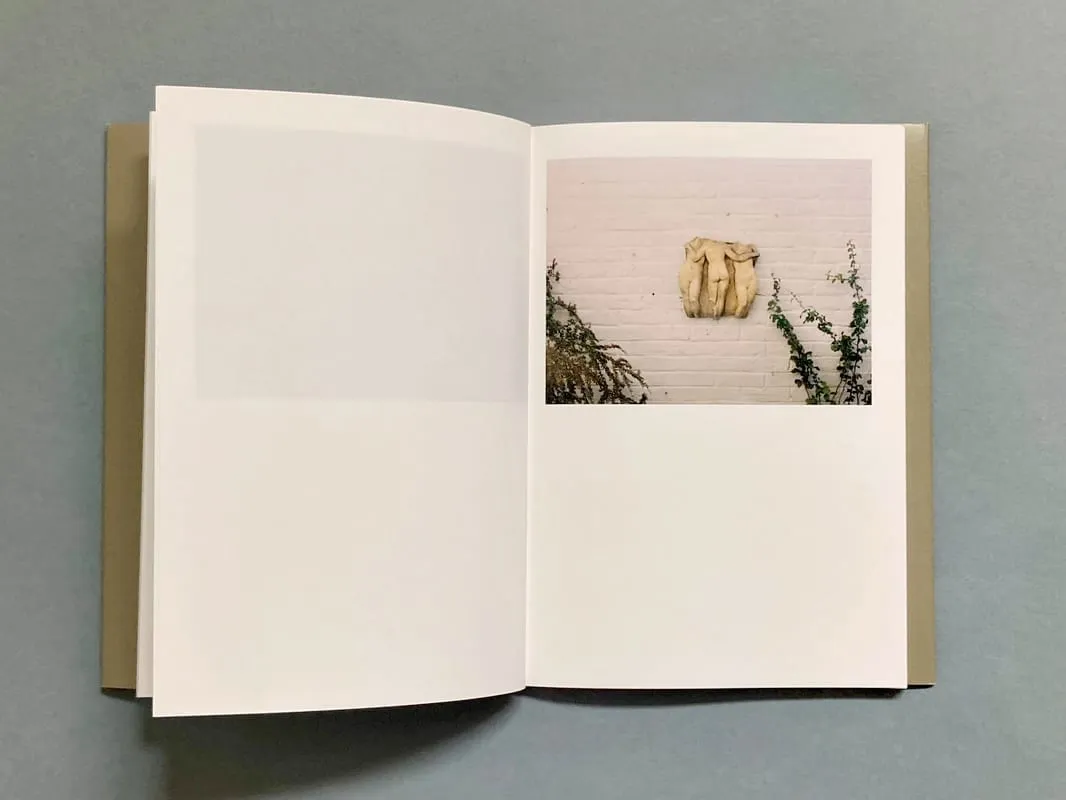 The work as a book: an open volume with a sand-coloured cover on a grey-blue surface, the left page blank and the right carrying the photograph of the relief.